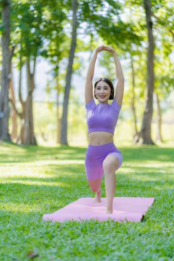 Genç Asyalı kadın egzersiz ve sağlık için bahçede yoga yapıyor. Parkta Asyalı kadın yoga yapıyor ve yazın yeşil parkta spor kıyafetleriyle rahatlıyor.