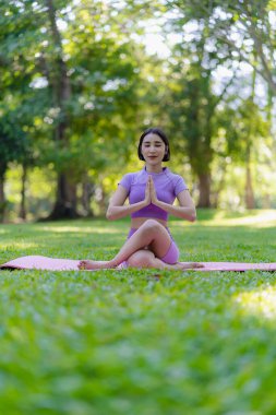 Genç Asyalı kadın egzersiz ve sağlık için bahçede yoga yapıyor. Parkta Asyalı kadın yoga yapıyor ve yazın yeşil parkta spor kıyafetleriyle rahatlıyor.