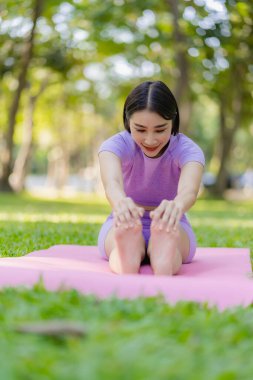 Genç Asyalı kadın egzersiz ve sağlık için bahçede yoga yapıyor. Parkta Asyalı kadın yoga yapıyor ve yazın yeşil parkta spor kıyafetleriyle rahatlıyor.