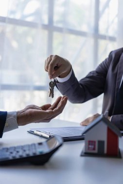 Emlakçı sigorta satış temsilcisi ve genç bir Asyalı işadamı satış sözleşmesini imzaladıktan sonra ev alıcısının anahtarlarını ve model bir evi teslim ediyorlar. dikey resim