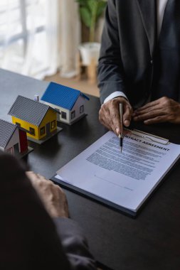 Sigortacı, ev kiralamak isteyen bir kalemi işaret ediyor. Ev almak için bir kontrat imzalamış. Bir ev ve ev satın alma sözleşmesi yapan bir emlakçı. Dikey resim.