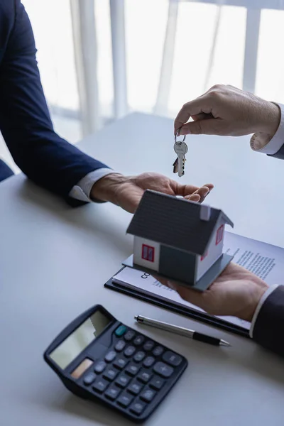 real estate agent insurance sales representative And a young Asian businessman handing over the keys to the home buyer and a model house after signing the sale contract at the table. vertical image