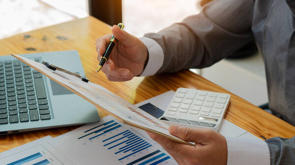 Accountant holding pen and using calculator doing company taxes on wooden table in office tax, accounting, statistics and analytical research concept, business finance