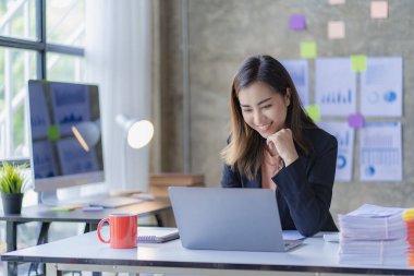 İnternette çalışan ve dizüstü bilgisayar ve mali belgelerle finansal veri planlayan Asyalı kadın, ev işkadını ve finans planlamacısı