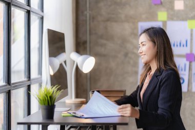 İnternette çalışan ve dizüstü bilgisayar ve mali belgelerle finansal veri planlayan Asyalı kadın, ev işkadını ve finans planlamacısı