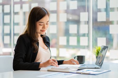 İnternette çalışan ve dizüstü bilgisayar ve mali belgelerle finansal veri planlayan Asyalı kadın, ev işkadını ve finans planlamacısı