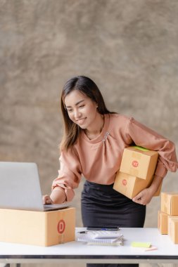 İnternette araştırma yapan Asyalı kadın ürünler alıyor, kutularla çalışıyor. çevrimiçi ofis işi küçük bir ortam kuruluşu dikey görüntüsü