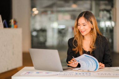 Masada dizüstü bilgisayarla çalışan iş kadını Asyalı kadın muhasebeci ya da bankacı ofisteki finans ve finans ekonomisi kavramını hesaplıyor.