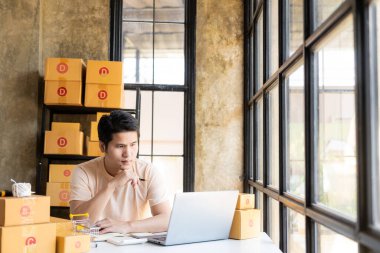 Asyalı bir adam internetten bilgisayarla, internet üzerinden ve e-ticaretle müşteri siparişi alıyor. Ev ürünleri sat