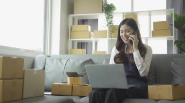 Ev telefonlu, bilgisayarlı, tabletli, güverteli (KOBİ) akıllı telefonlu kadın girişimci. Asyalı kadınların evde müşteri siparişlerini kontrol etmesi, müşterilere mal teslimatı..