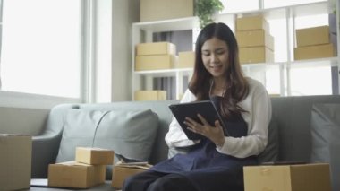 Ev telefonlu, bilgisayarlı, tabletli, güverteli (KOBİ) akıllı telefonlu kadın girişimci. Asyalı kadınların evde müşteri siparişlerini kontrol etmesi, müşterilere mal teslimatı..