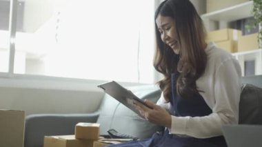 Ev telefonlu, bilgisayarlı, tabletli, güverteli (KOBİ) akıllı telefonlu kadın girişimci. Asyalı kadınların evde müşteri siparişlerini kontrol etmesi, müşterilere mal teslimatı..