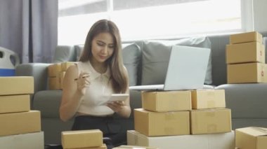 Ev telefonlu, bilgisayarlı, tabletli, güverteli (KOBİ) akıllı telefonlu kadın girişimci. Asyalı kadınların evde müşteri siparişlerini kontrol etmesi, müşterilere mal teslimatı..