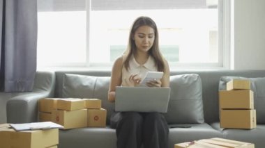 Ev telefonlu, bilgisayarlı, tabletli, güverteli (KOBİ) akıllı telefonlu kadın girişimci. Asyalı kadınların evde müşteri siparişlerini kontrol etmesi, müşterilere mal teslimatı..