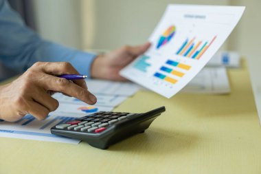 Belgelerle, mali grafiklerle ve faturalarla çalışan iş yerinde dizüstü bilgisayarla muhasebe hesaplarını uzaktan analiz eden bir işadamı..