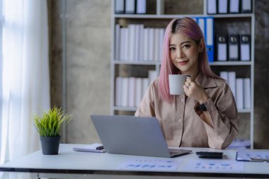 Finans ofisinde çalışan genç Asyalı muhasebeci hesap makinesi ve finansal belgeler kullanarak satış raporlarını yönetiyor..