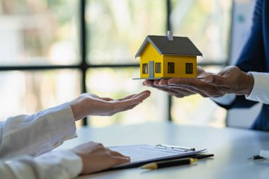 Emlakçılar faiz oranları öneriyor, ev satın alma anlaşmasının şartlarını tartışıyorlar ve müşterilerden sözleşmeyi yasallaştırmak için evrakları imzalamalarını istiyorlar..