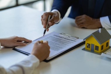 Emlakçılar faiz oranları öneriyor, ev satın alma anlaşmasının şartlarını tartışıyorlar ve müşterilerden sözleşmeyi yasallaştırmak için evrakları imzalamalarını istiyorlar..