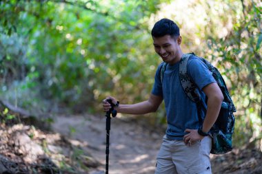 Yorgun ve yorgun Asyalı erkek gezgin yürüyüş takımları ve sırt çantasıyla dinleniyor. Yürüyüşe ve turizm konseptine ara verin..