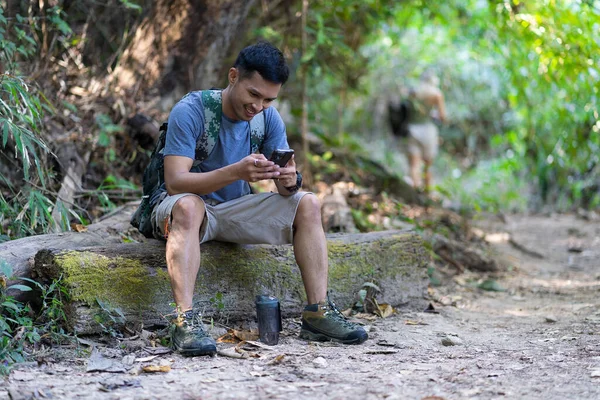 stock image Handsome asian young male traveler with backpack, holding walking stick and hiking stick, standing in the forest with happiness, freedom in summer vacation, travel concept.