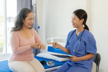 Asyalı yaşlı kadın mutlulukla gülümsüyor ve masada yaşlı bir kadınla konuşan bir kadın doktor tarafından teselli ediliyor. Muayenenin, muayenenin ve tedavinin sonuçlarını anlatıyor.