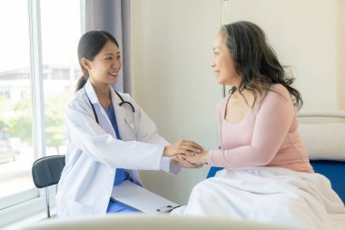 Asyalı yaşlı kadın mutlulukla gülümsüyor ve masada yaşlı bir kadınla konuşan bir kadın doktor tarafından teselli ediliyor. Muayenenin, muayenenin ve tedavinin sonuçlarını anlatıyor.