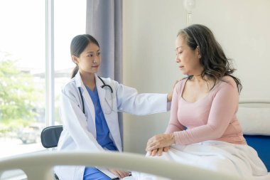 Asyalı yaşlı kadın mutlulukla gülümsüyor ve masada yaşlı bir kadınla konuşan bir kadın doktor tarafından teselli ediliyor. Muayenenin, muayenenin ve tedavinin sonuçlarını anlatıyor.