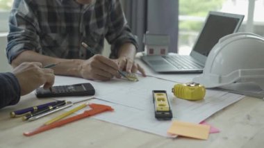 İnşaat mühendisi ekibi mimar ve ustabaşıyla birlikte Mavi Yazıcı 'ya bakın ve binanın inşaatını planlayın. Ofiste, masa 4k 'nin üzerinde aletlerle.