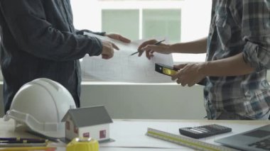 İnşaat mühendisi ekibi mimar ve ustabaşıyla birlikte Mavi Yazıcı 'ya bakın ve binanın inşaatını planlayın. Ofiste, masa 4k 'nin üzerinde aletlerle.