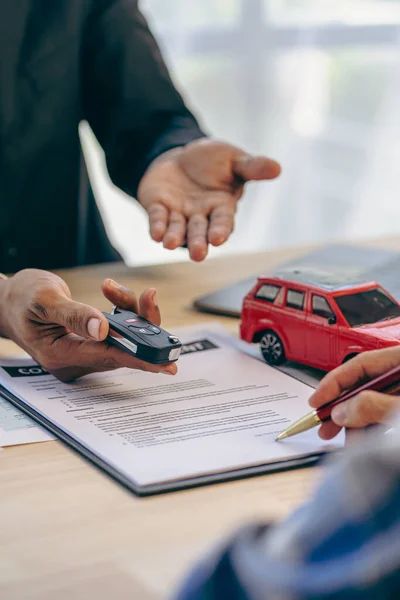 Employee of the rental car company handing over the keys to the renter after discussing the details and conditions of the contract with the customer who signed the insurance.