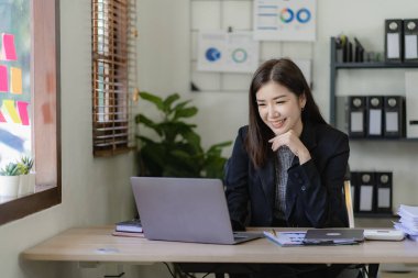 Masa, rapor, muhasebe, istatistik ve analitik araştırma kavramında finansal matematik yapmak için dizüstü bilgisayar ve hesap makinesi finansman grafikleri kullanan Asyalı güzel bir iş kadını.