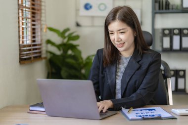 Masa, rapor, muhasebe, istatistik ve analitik araştırma kavramında finansal matematik yapmak için dizüstü bilgisayar ve hesap makinesi finansman grafikleri kullanan Asyalı güzel bir iş kadını.