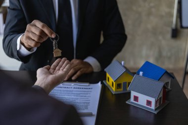 Emlakçılar konut satın almak ya da kiralamak için sözleşme teklif ediyorlar. Modeli elinde tutan bir işadamı ev sigortası olan küçük bir bina.
