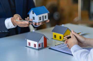 Emlakçılar konut satın almak ya da kiralamak için sözleşme teklif ediyorlar. Modeli elinde tutan bir işadamı ev sigortası olan küçük bir bina.