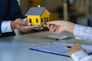 Emlakçılar konut satın almak ya da kiralamak için sözleşme teklif ediyorlar. Modeli elinde tutan bir işadamı ev sigortası olan küçük bir bina.