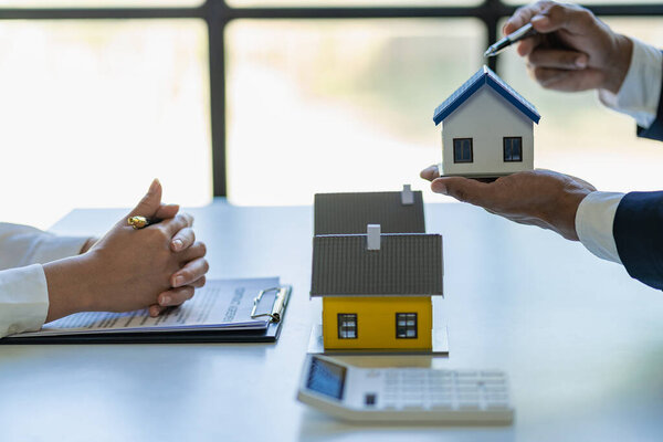 Real estate agents offer contracts to buy or rent housing. Businessman holding model small building house with property insurance at table in home sales office
