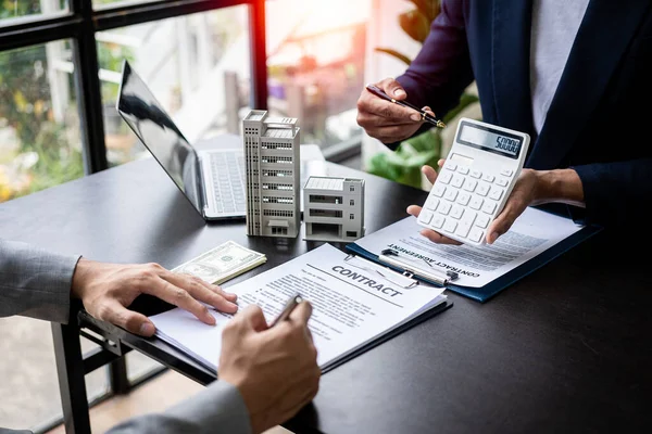 stock image Real estate agents offer contracts to buy or rent housing. Businessman holding model small building house with property insurance at table in home sales office