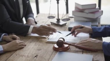 Çok ırklı avukatlar belgelerle çalışıyor ve hukuk bürosundaki konferans masasında tartışıyorlar. Masada terazili ve çekiçli adalet kavramı.