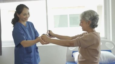 Genç bayan fizyoterapist, kas egzersizi ve fizyoterapi için direnç bantları kullanan gri saçlı yaşlı kadına kol hareketlerini gösteriyor.