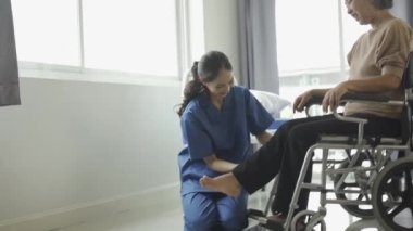 Genç bayan fizyoterapist konuşuyor ve kas egzersizi ve fizyoterapi için direnç bantları kullanan gri saçlı yaşlı kadına ayak bileği hareketlerini gösteriyor.