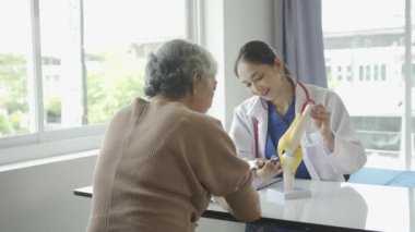 Kadın doktor yaşlı hastaya danışmanlık yapıyor ve klinikte reçete yazıyor. Osteoartrit uzmanı, kadın doktor, yaşlıların tıbbi geçmişlerine ve konuşmalarına bakıyor, tavsiyelerde bulunuyor.