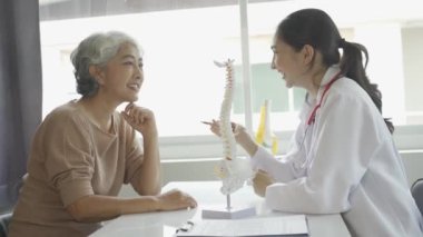 Kadın doktor yaşlı hastaya danışmanlık yapıyor ve klinikte reçete yazıyor. Osteoartrit uzmanı, kadın doktor, yaşlıların tıbbi geçmişlerine ve konuşmalarına bakıyor, tavsiyelerde bulunuyor.