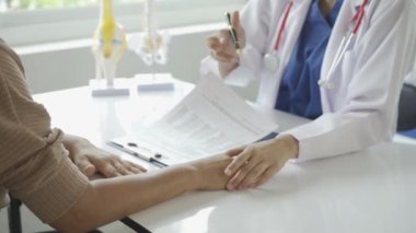 Kadın doktor yaşlı hastaya danışmanlık yapıyor ve klinikte reçete yazıyor. Osteoartrit uzmanı, kadın doktor, yaşlıların tıbbi geçmişlerine ve konuşmalarına bakıyor, tavsiyelerde bulunuyor.