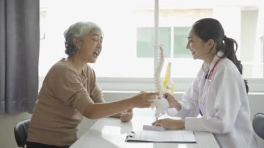 Kadın doktor yaşlı hastaya danışmanlık yapıyor ve klinikte reçete yazıyor. Osteoartrit uzmanı, kadın doktor, yaşlıların tıbbi geçmişlerine ve konuşmalarına bakıyor, tavsiyelerde bulunuyor.