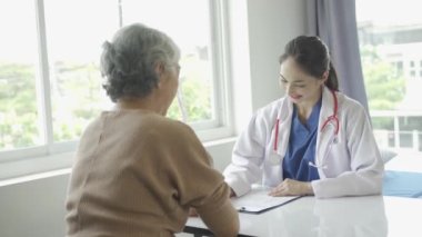 Kadın doktor yaşlı hastaya danışmanlık yapıyor ve klinikte reçete yazıyor. Osteoartrit uzmanı, kadın doktor, yaşlıların tıbbi geçmişlerine ve konuşmalarına bakıyor, tavsiyelerde bulunuyor.