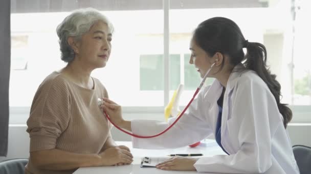 病院での高齢女性患者の肺や心拍数を確認するために聴診器を使用する女性医師トーク療法は 医療の概念を奨励しています — ストック動画