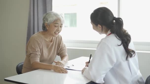 女医生咨询老年病人 在诊所的桌子旁开药方 女医生 查看老年人的病史 并提出建议 — 图库视频影像