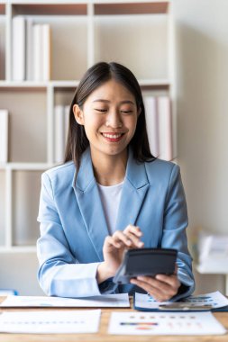 İş verilerini, muhasebe belgelerini ve bilgisayarlarını hesaplamak için finansal muhasebe ve hesap makinesi üzerinde çalışan Asyalı kadın muhasebeci elinde kalem tutuyor.