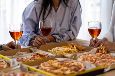 Meslektaşlar pizza partisinde öğle yemeği yer, çeşitli pizzalar yer ve kırsal ahşap masada kırmızı şarap içerek fast food öğle yemeğini kutlarlar.