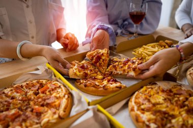 Meslektaşlar pizza partisinde öğle yemeği yer, çeşitli pizzalar yer ve kırsal ahşap masada kırmızı şarap içerek fast food öğle yemeğini kutlarlar.